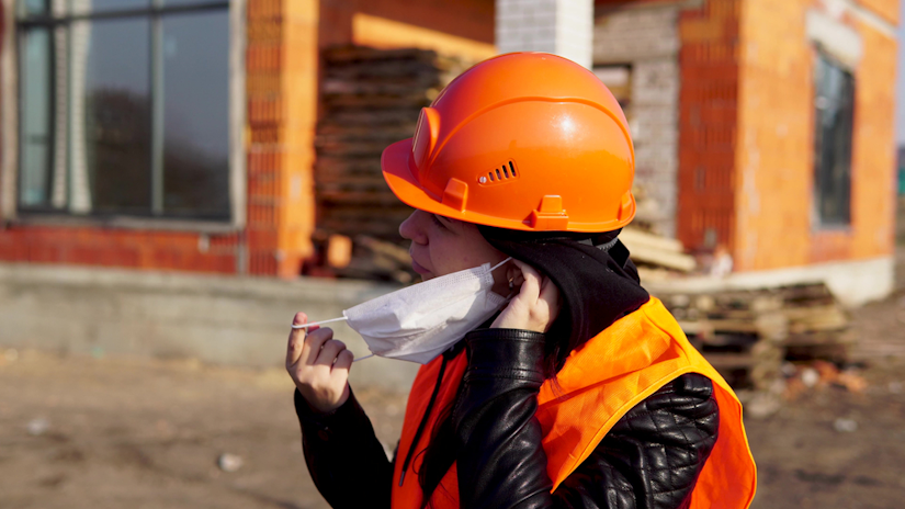 Construction worker in an orange vest and hard hat putting on a face mask