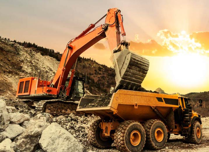 Heavy duty excavator dumping rocks into a construction dump truck